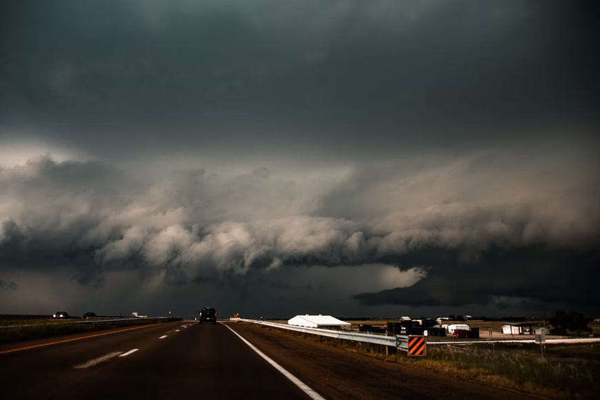 A large black tornado building up at the end of a highway