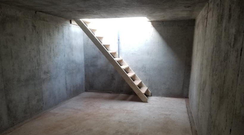 The inside of a concrete underground bunker with a ladder.