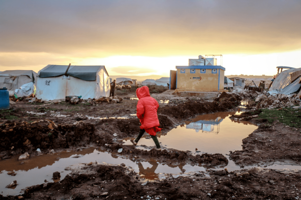 Unrecognizable girl walks over mud against shelter homes.