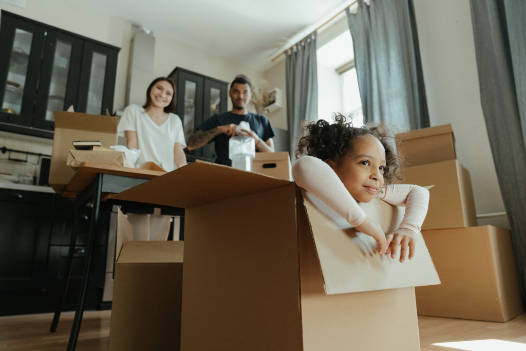 Little girl sitting in a box with her parents in the background