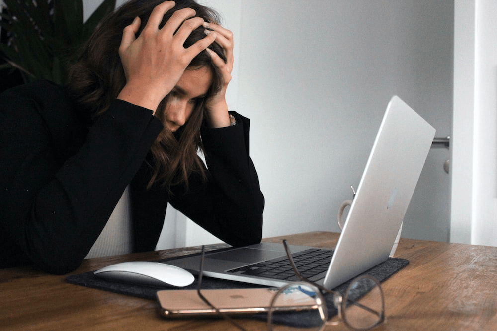 A woman sitting extremely stressed in front of her laptop. 