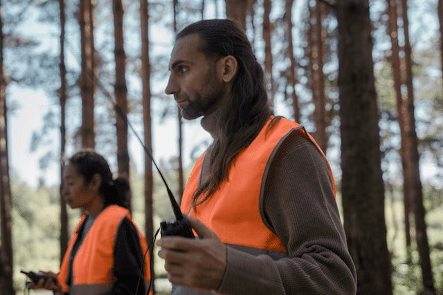 A person in an orange vest holding a walkie-talkie.