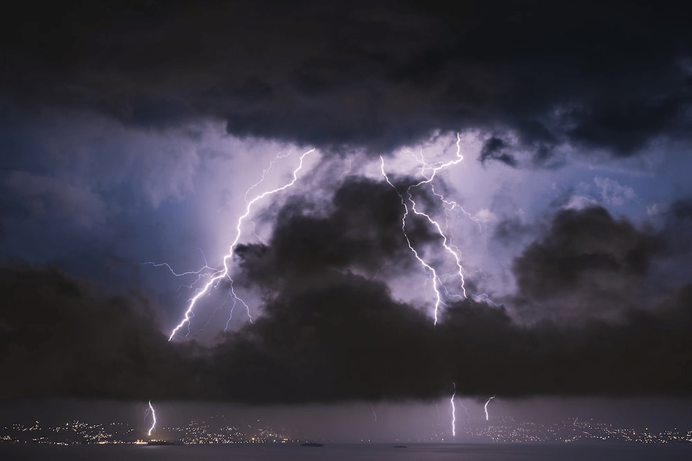 a large dark cloud over the city with lighting and thunder striking.