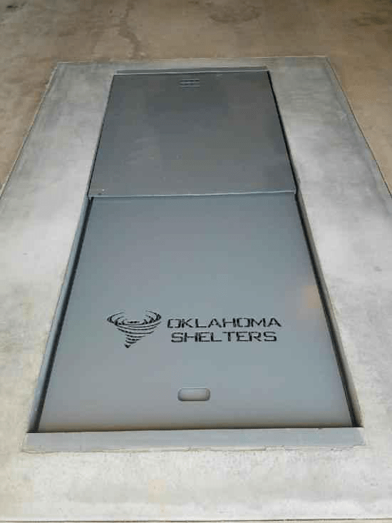 A picture showing a gray underground shelter with “OKLAHOMA SHELTERS” engraved alongside a tornado depiction on it