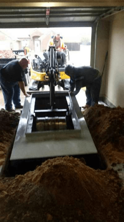 A team of professional installers lowering a garage storm shelter into the ground using a crane.