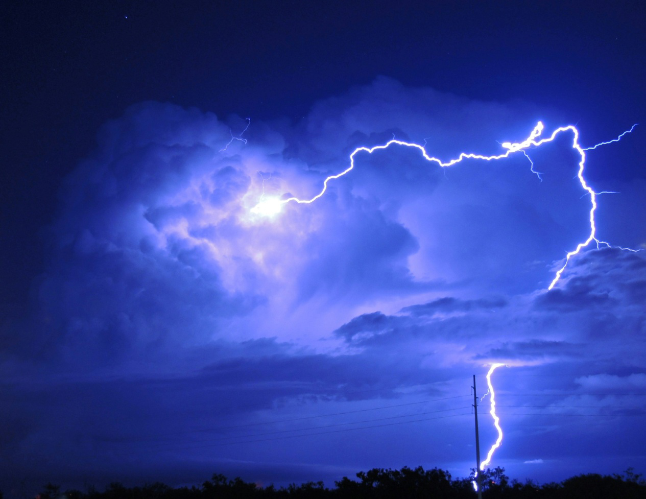 Bright lightning strikes, illuminating the night sky over a neighborhood