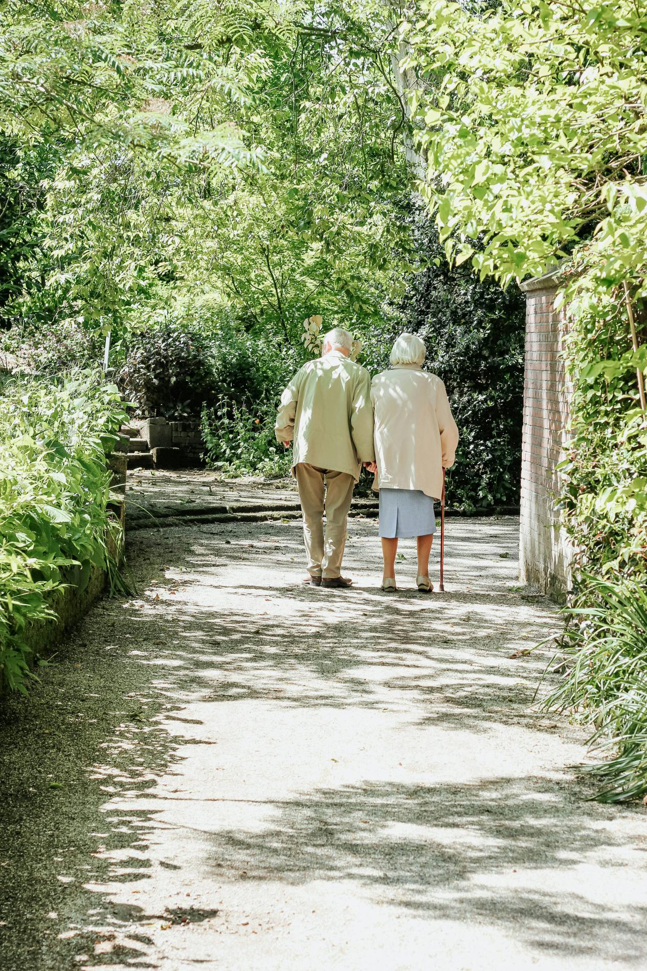 An elderly couple walking together outdoors, with one of them having a cane