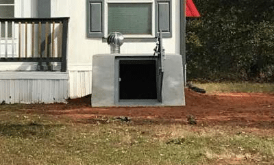 Above-ground residential storm shelter with exterior entry installed beside a home.