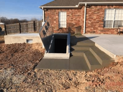 Backyard underground storm shelter with concrete stair access beside a brick home