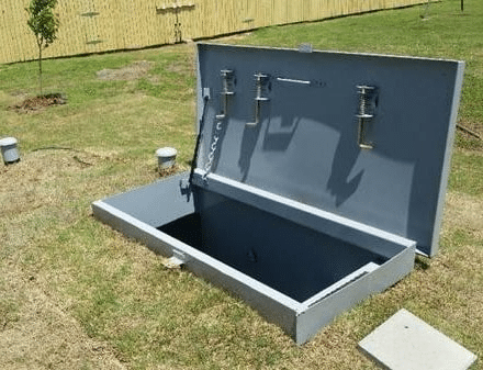 Underground storm shelter with open lid.