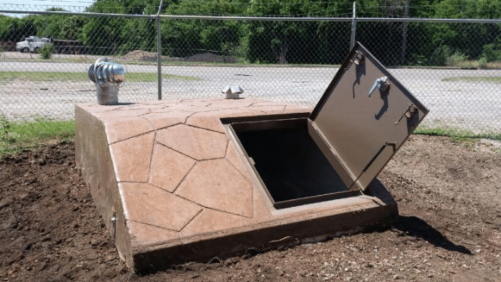 Underground storm shelter with open entry door and ventilation system.