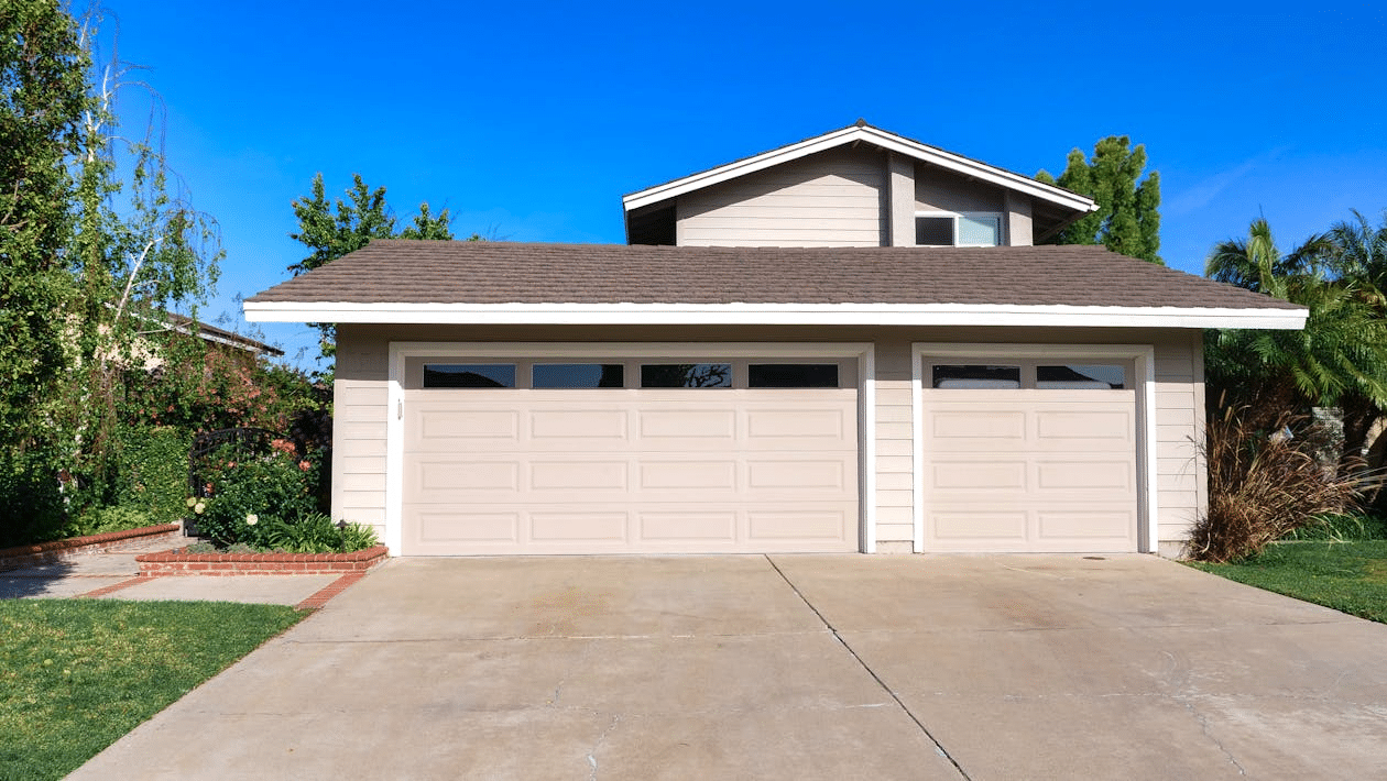 Exterior of a suburban home with a double garage and a For Sale sign on the front lawn