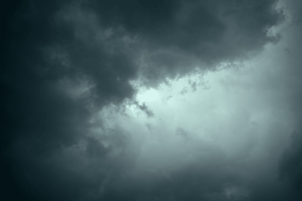 Ominous dark storm cloud covering most of a daytime sky with light breaking through