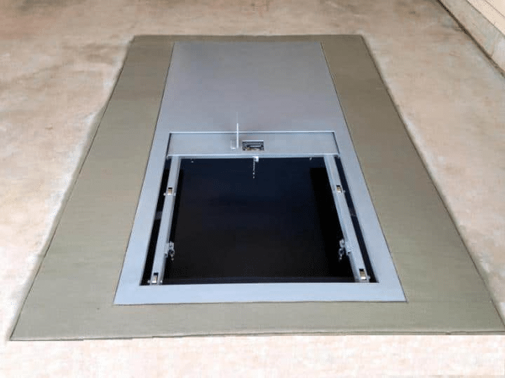 A picture shows an installed underground storm shelter with a metal lid that is partially open.