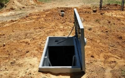A picture shows an open underground storm shelter hatch, with a metal frame and lid.
