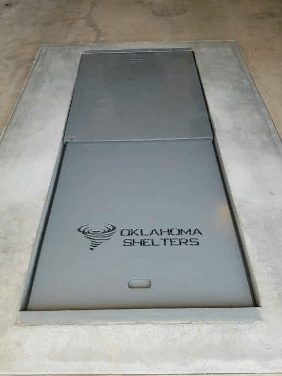 A gray rectangular underground garage shelter hatch, with "OKLAHOMA SHELTERS" on its lower panel.