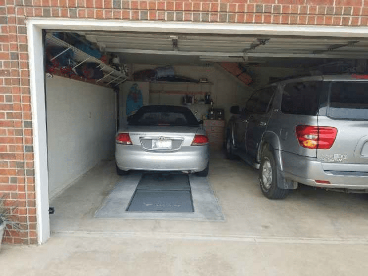 An image shows a silver car parked over an underground storm shelter entrance.