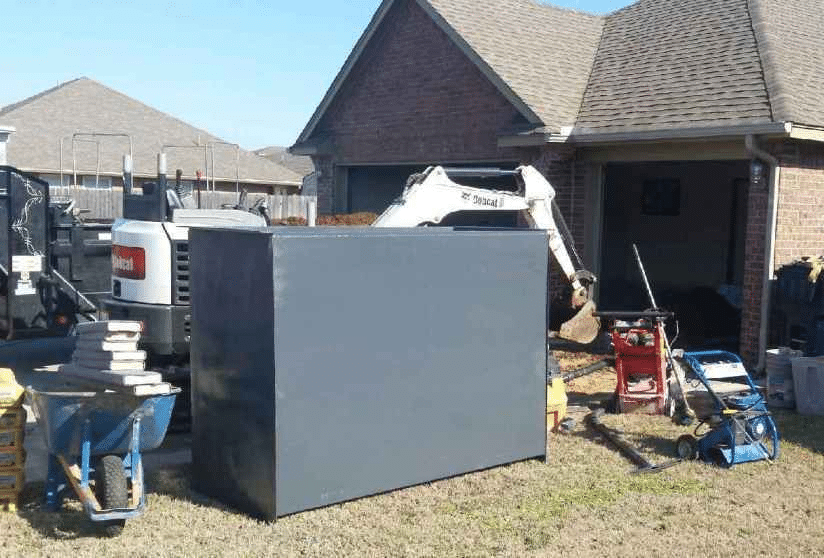 Large above-ground safe room being installed beside a residential home with equipment and tools on site.