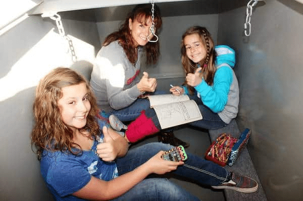 A picture shows an adult and two children comfortably seated inside an underground garage storm shelter.