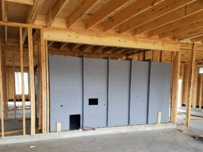 An image shows a wooden wall framing and pre-installed gray panels of a storm shelter.