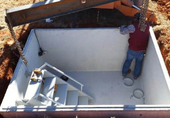 An image shows a concrete underground tornado shelter, with a man standing inside near the steps