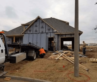 An image shows a new house under construction, framed with scaffolding and two workers installing a storm shelter