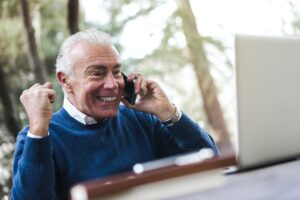 An excited elderly man on call while looking ahead at a laptop