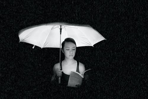 Grayscale image of a woman reading a book while holding an umbrella