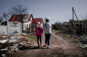two girls walking past a destroyed house