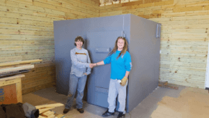 Two women shaking hands in front of a steel safe room.