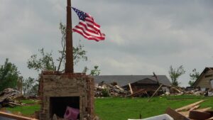 Destruction from a tornado can be seen in the background of the flag.