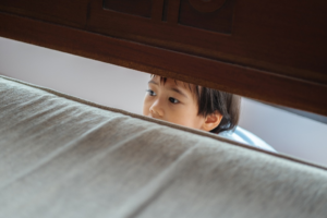 A kid hiding behind a bed during a storm.