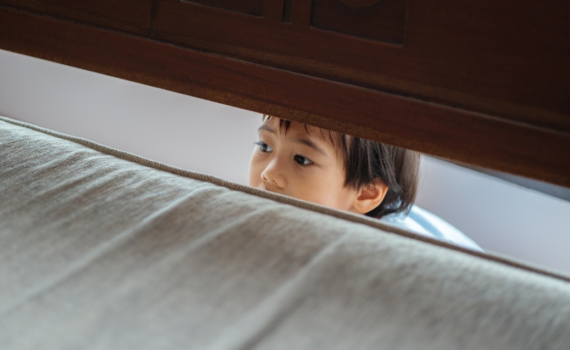 A kid hiding behind a bed during a storm.